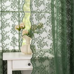 a vase with flowers sitting on a table in front of a green curtained window