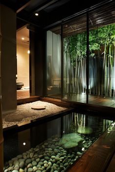 an indoor pond with rocks and bamboo trees in the background, surrounded by glass walls