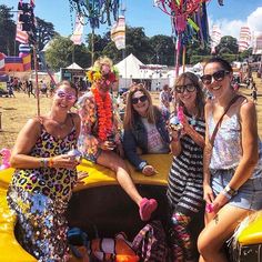 four women are sitting in the back of a yellow car at an outdoor festival with decorations on it