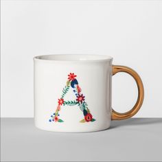 a white coffee mug with a gold handle and floral letter on the inside, sitting on a table