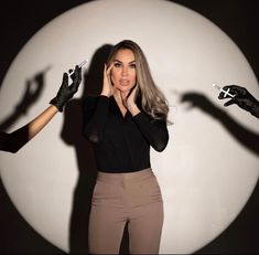 a woman in black shirt and gloves holding hands up to her face with shadow on the wall behind her