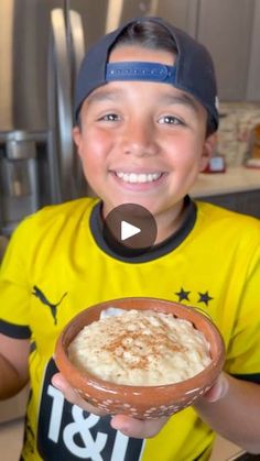 a young boy holding a bowl of food in his hand and smiling at the camera