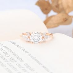 an engagement ring with three stones sits on top of a book, next to some leaves