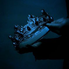 a person holding a tiara in their hand with blue light shining on the background