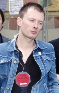 a young man wearing a denim jacket with a red tag on his shirt and black t - shirt