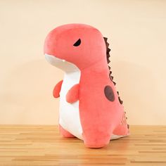 a pink dinosaur stuffed animal sitting on top of a wooden floor next to a wall