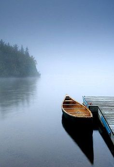 a small boat sitting on top of a lake next to a wooden dock in the fog