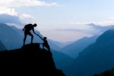 two people helping each other up on top of a mountain