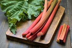 rhubarb stalks on a cutting board next to green leafy greens and leaves