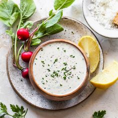 a bowl of white sauce on a plate with lemon and radishes