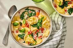 two bowls filled with pasta and spinach on top of a table