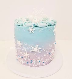 a frosted blue and white cake with snowflakes on the top is sitting on a plate