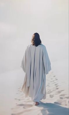 a person walking in the sand with their back to the camera, wearing a white robe