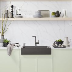 a kitchen with green cabinets and white marble counter tops is pictured in this image, there are plants on the shelves above the sink