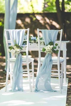 two white chairs with blue sashes and flowers on them are set up for an outdoor ceremony