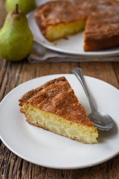 a piece of pie on a plate with a fork next to it and two pears in the background