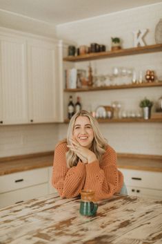 a woman sitting at a kitchen table with her hands on her chest and smiling for the camera