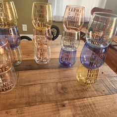 five wine glasses with different sayings on them sitting on a wooden table in front of a window