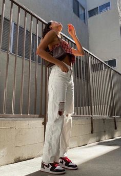 a woman standing on the sidewalk with her hands in her pockets and wearing ripped jeans