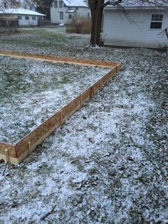 a wooden bed frame in the middle of a yard covered in snow and grass with a house in the background