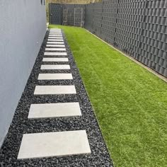 an outdoor walkway with stepping stones in the grass next to a wall and green lawn