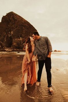 a man and woman kissing on the beach in front of a rock formation at sunset