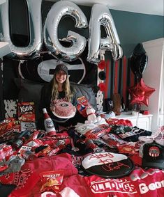 a woman sitting in front of a bed covered in red shirts and balloons with the word uga on it