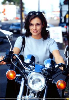 a woman sitting on top of a motorcycle in the street with her hand on the handlebars