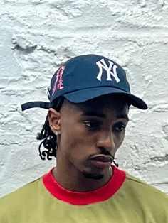 a young man wearing a new york yankees hat and yellow t - shirt, standing in front of a white brick wall