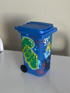 a blue trash can sitting on top of a white table next to a black object