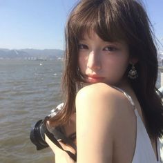 a woman with long brown hair standing in front of the water