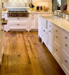 a large kitchen with white cabinets and wood flooring, along with marble counter tops