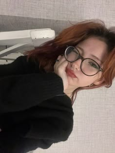 a woman with red hair and glasses laying on a bed