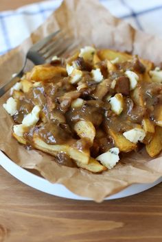 a white plate topped with fries covered in gravy next to a knife and fork