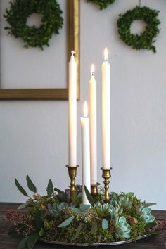 four candles are lit on a table with succulents and greenery