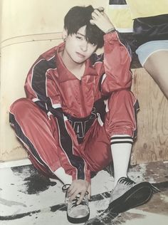 a young man sitting on the ground with his foot up to his head, wearing a red and black outfit