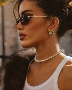 a woman wearing sunglasses and a white tank top is looking off to the side with her hair in a bun