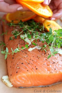 someone cutting up some food on top of a piece of paper with orange slices and herbs