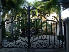 an iron gate in front of palm trees and a driveway with a walkway leading to it