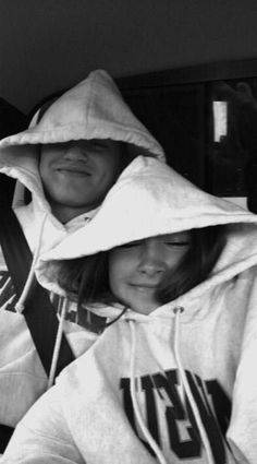 two people sitting in the back seat of a car wearing hoods and sweatshirts