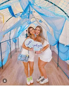 two young women posing for a photo under a blue netted canopy with the words goodbye written on it