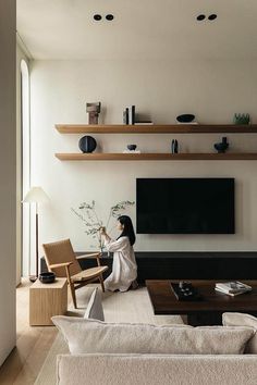 a woman sitting on the floor in front of a flat screen tv with shelves above her