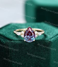 an engagement ring with a pink and blue stone surrounded by white diamonds on a green velvet box