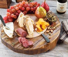 a wooden plate with meat, cheese and fruit on it next to two wine glasses