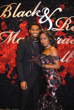 a man and woman standing next to each other in front of a black and red wall