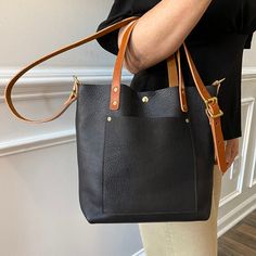 The Black Crossbody Leather Tote Bag  Back in Black! Our leather Crossbody Tote comes in this beautiful oil-tanned Black kodiac leather. This leather tote is sewn on the inside of the bag to evoke a more seamless look. This crossbody tote comes with a short, dark veg-tanned handle (intended to be carried by the hand) o Back In Black, Tanning Oil, Aging Beautifully, Leather Hide, Black Crossbody, Crossbody Tote, Back To Black, Leather Tote Bag, Full Grain Leather