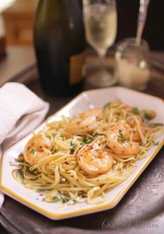 pasta with shrimp and parsley on a plate next to a bottle of wine in the background