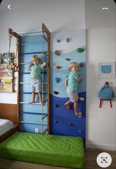 two young children climbing up and down the wall in a bedroom with green bedding