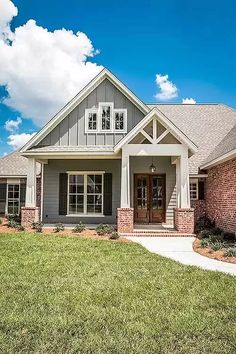 a gray and red brick house with white trim on the front door, windows, and grass in front of it