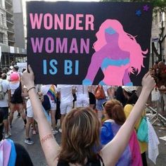 a woman holding up a sign that says wonder woman is bi